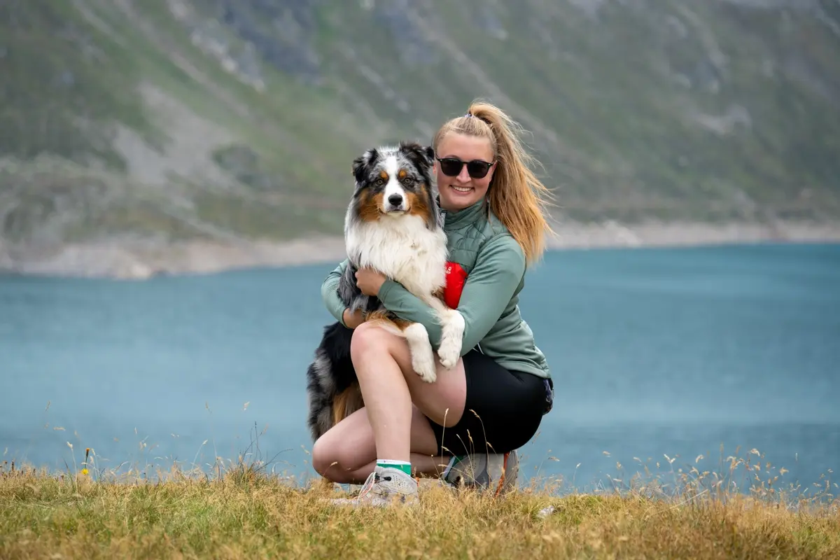 Mäddchen hockend mit einem Australian Shepherd im Arm vor einem See